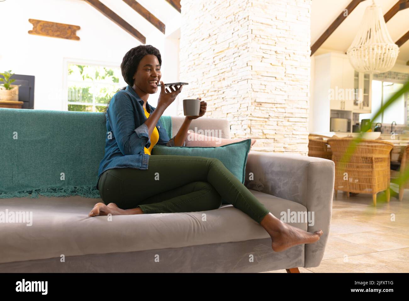 African american young woman sending voicemail through smart phone while having coffee at home Stock Photo