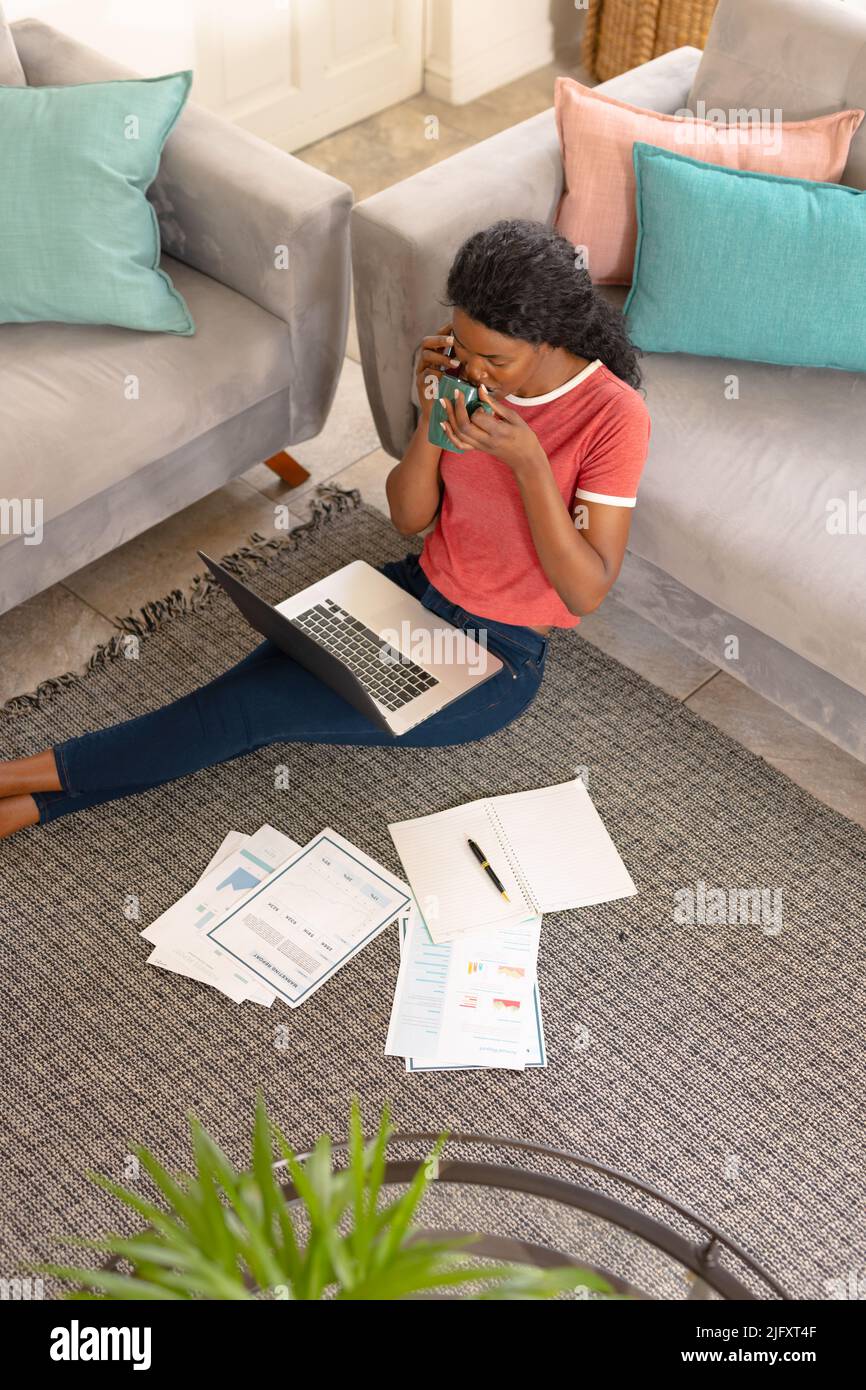 African american young female freelancer drinking coffee while working in living room at home Stock Photo