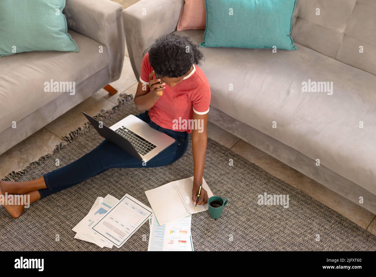 Young african american female freelancer discussing project while talking on smart phone by sofa Stock Photo