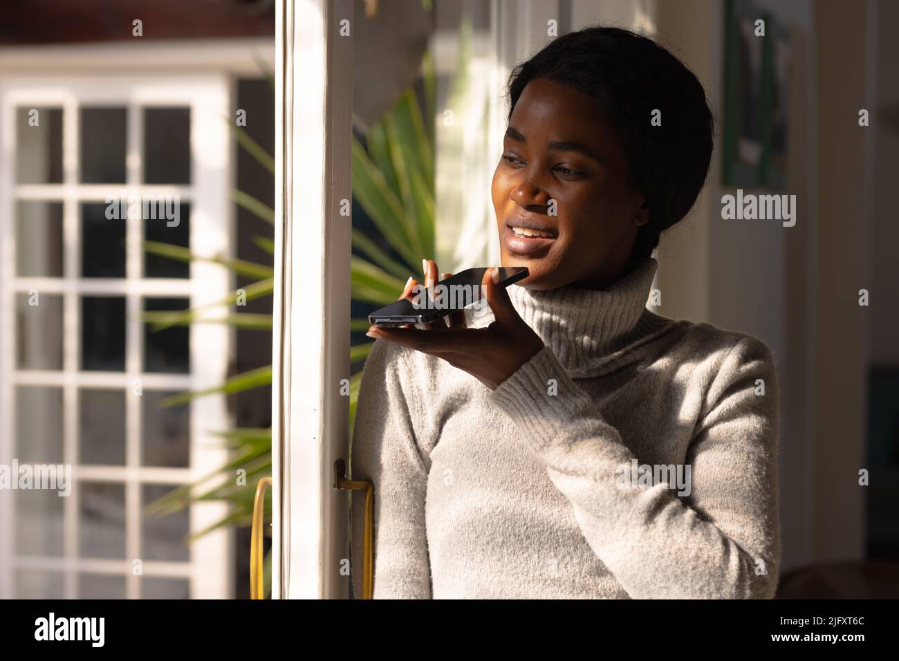 African american young woman sending voicemail through smart phone by window at home, copy space Stock Photo