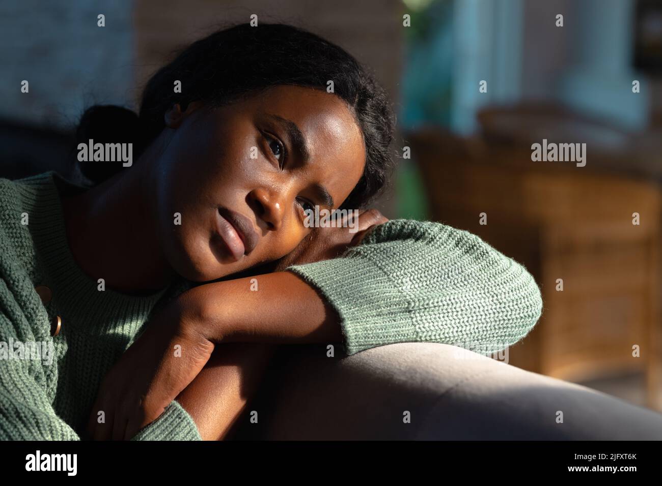 Lonely african american young woman looking away while resting head on sofa at home, copy space Stock Photo