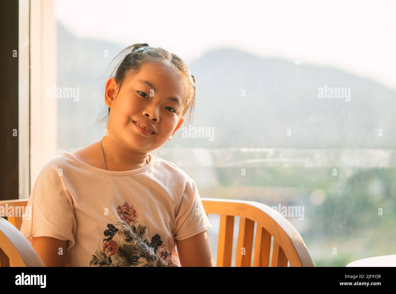 Portrait of Asian cute child girl sitting in front of mirror wall of a hotel, sunlight from the back. Child girl with smiling face, blank space for te Stock Photo