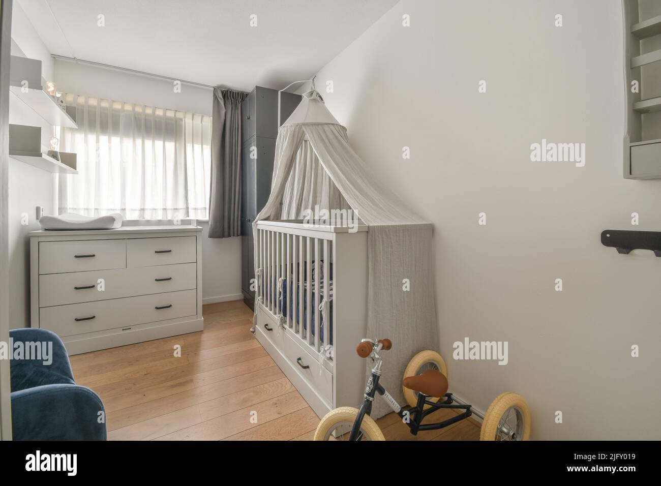 Interior of white room with baby crib and armchair near window with