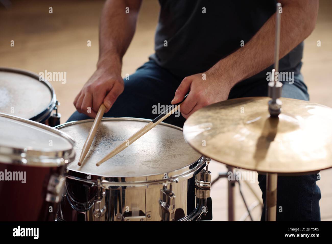 Closeup of man sitting behind drum kit and playing drums during