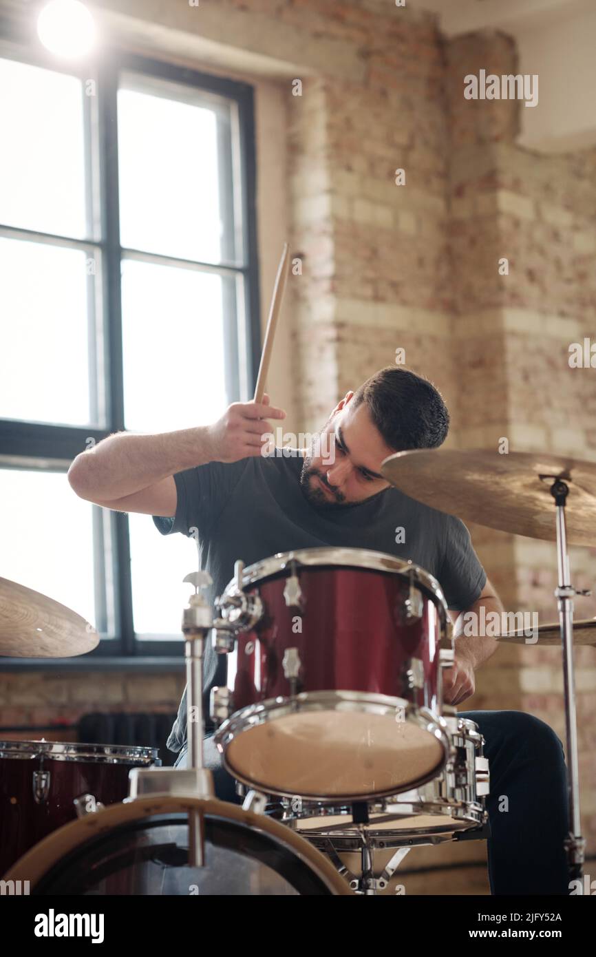 Young professional drummer playing drums with drumsticks sitting at
