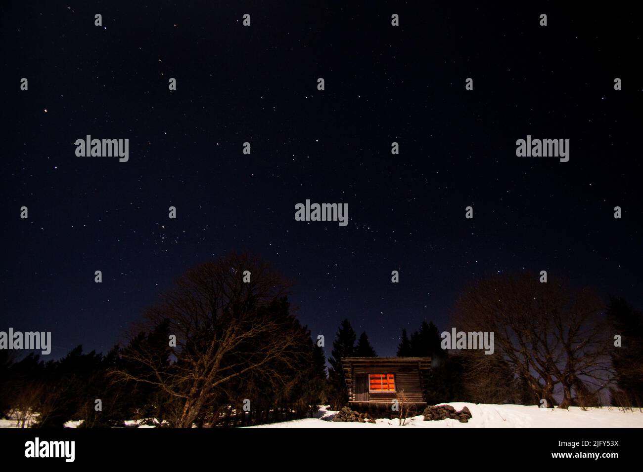 Log cabin shelter in the wild mountains at night with stellar sky during winter in Vosges, France Stock Photo