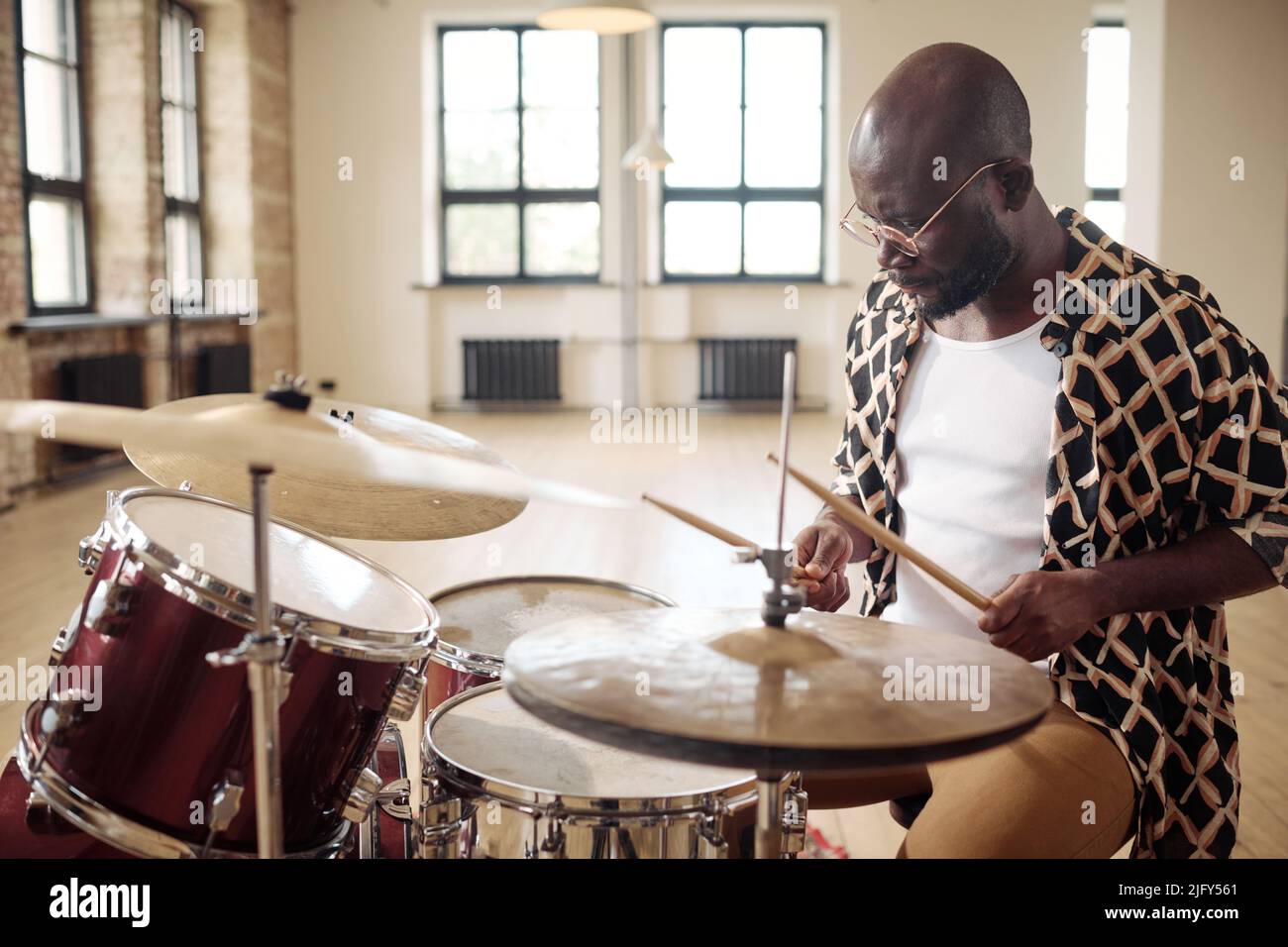 African young man drummer behind drum set playing the drums in studio