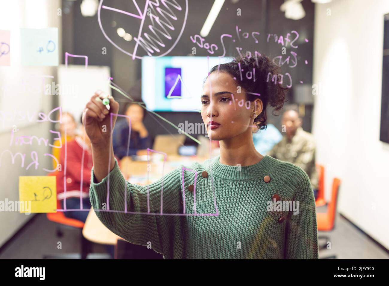 Confident biracial female app developer drawing chart on glass in board room Stock Photo