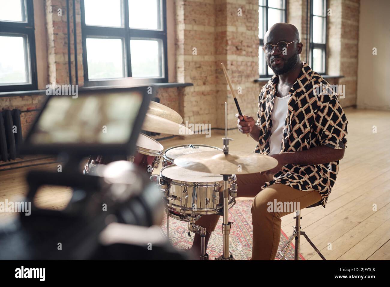 Portrait of African young drummer performing on drums on camera for online broadcasting at empty studio Stock Photo