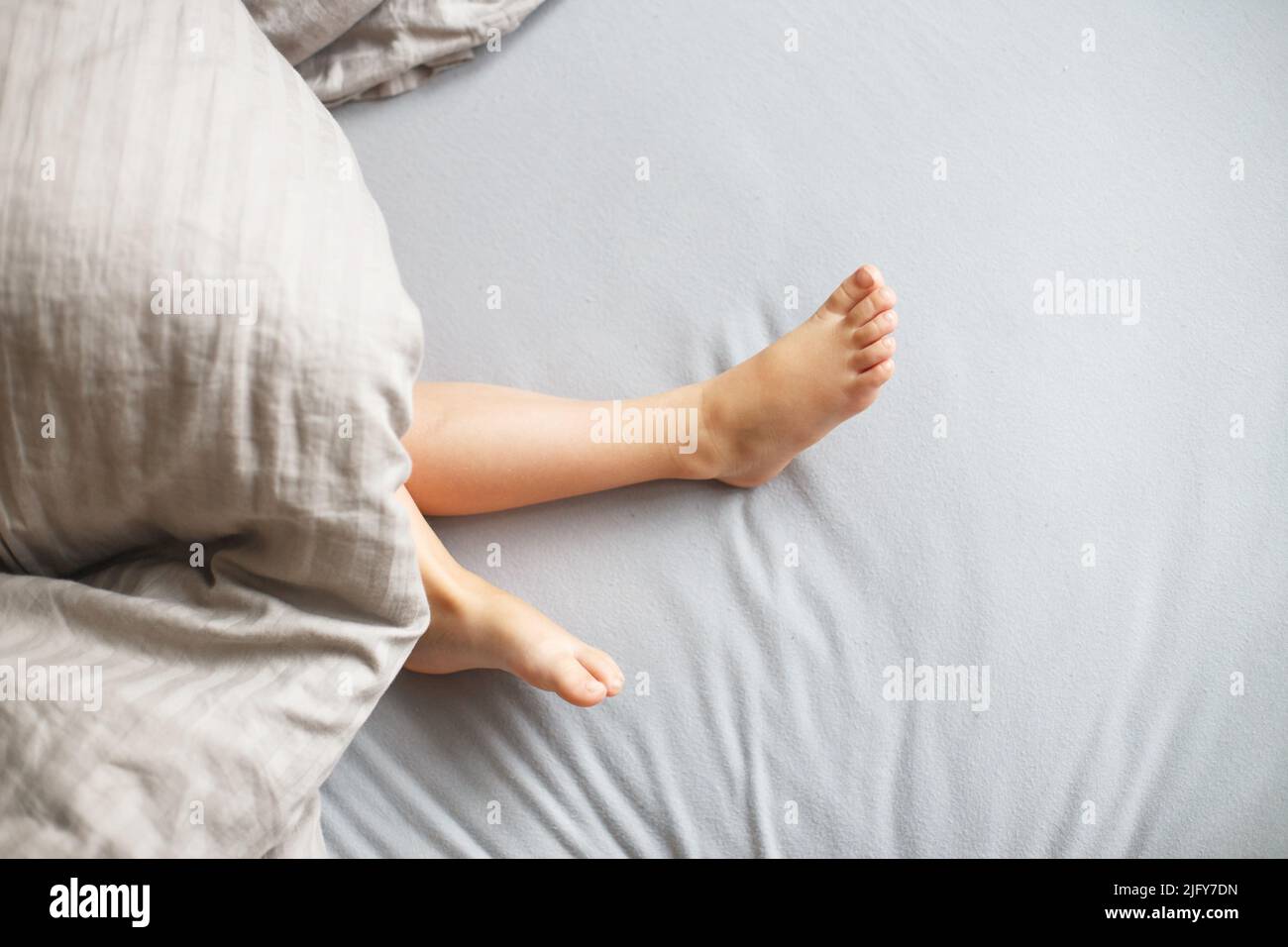 child sleep in the bed. baby's feet stick out from under the blanket