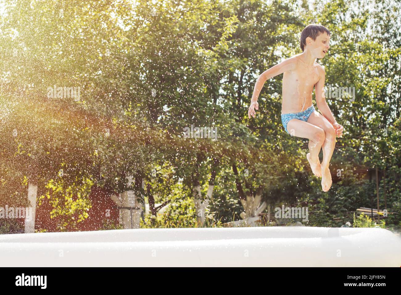 boy jumping into the swimming pool in the garden at summer. Stock Photo