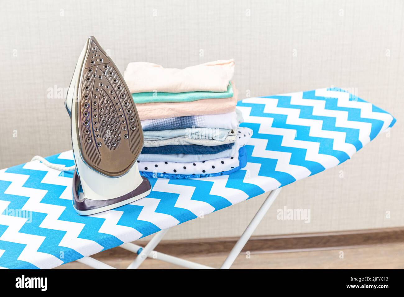 Folded ironed men's shirts lie next to the iron on the ironing board