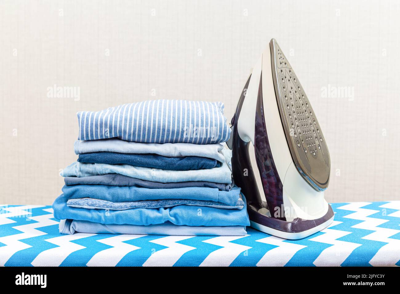 Folded ironed men's shirts lie next to the iron on the ironing board