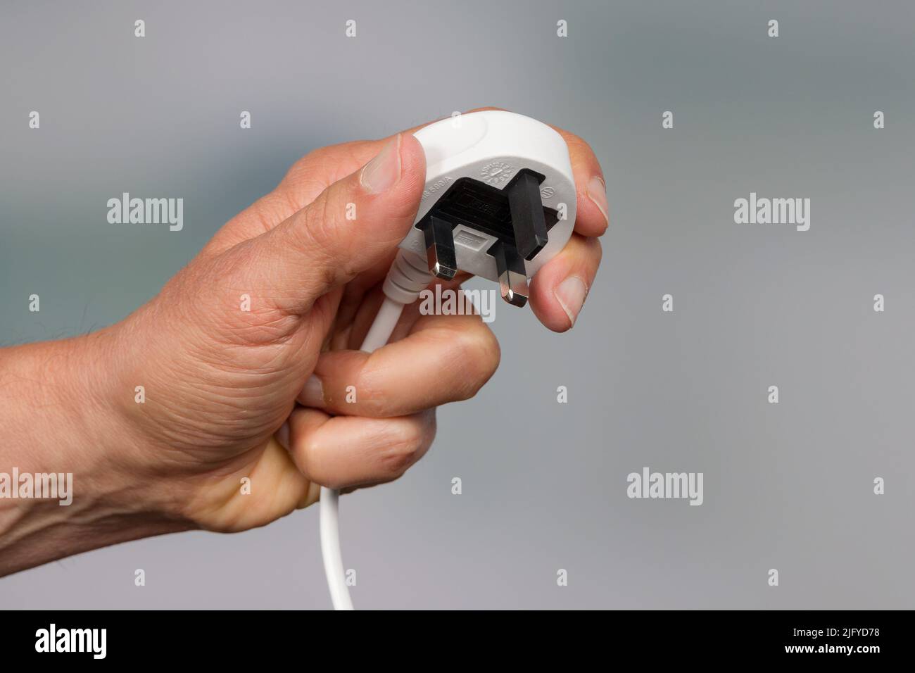 a hand is presenting a three pin power plug Stock Photo