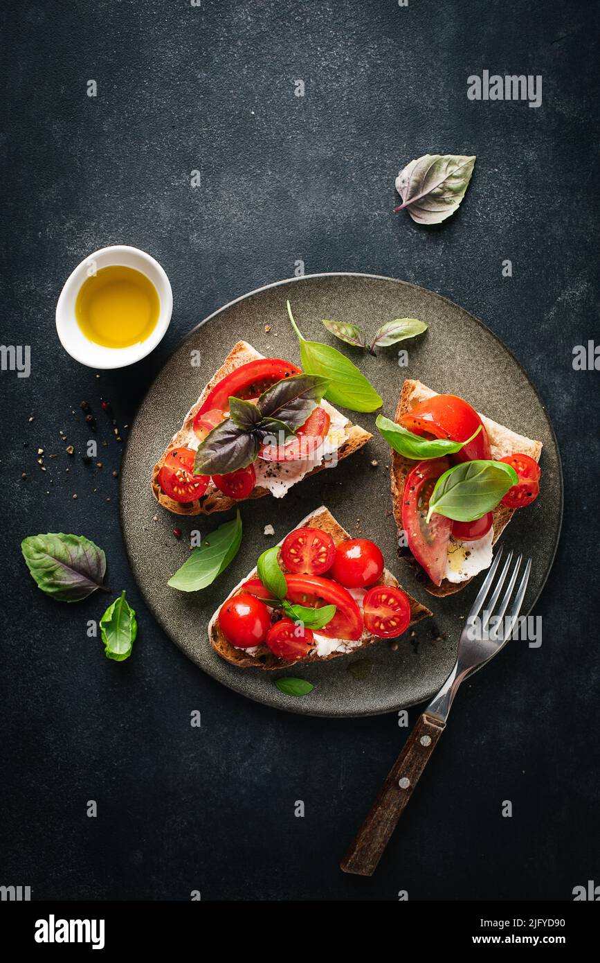 Tomato and ricotta cheese bruschetta topped with basil and EV olive oil. Top view. Italian food Stock Photo