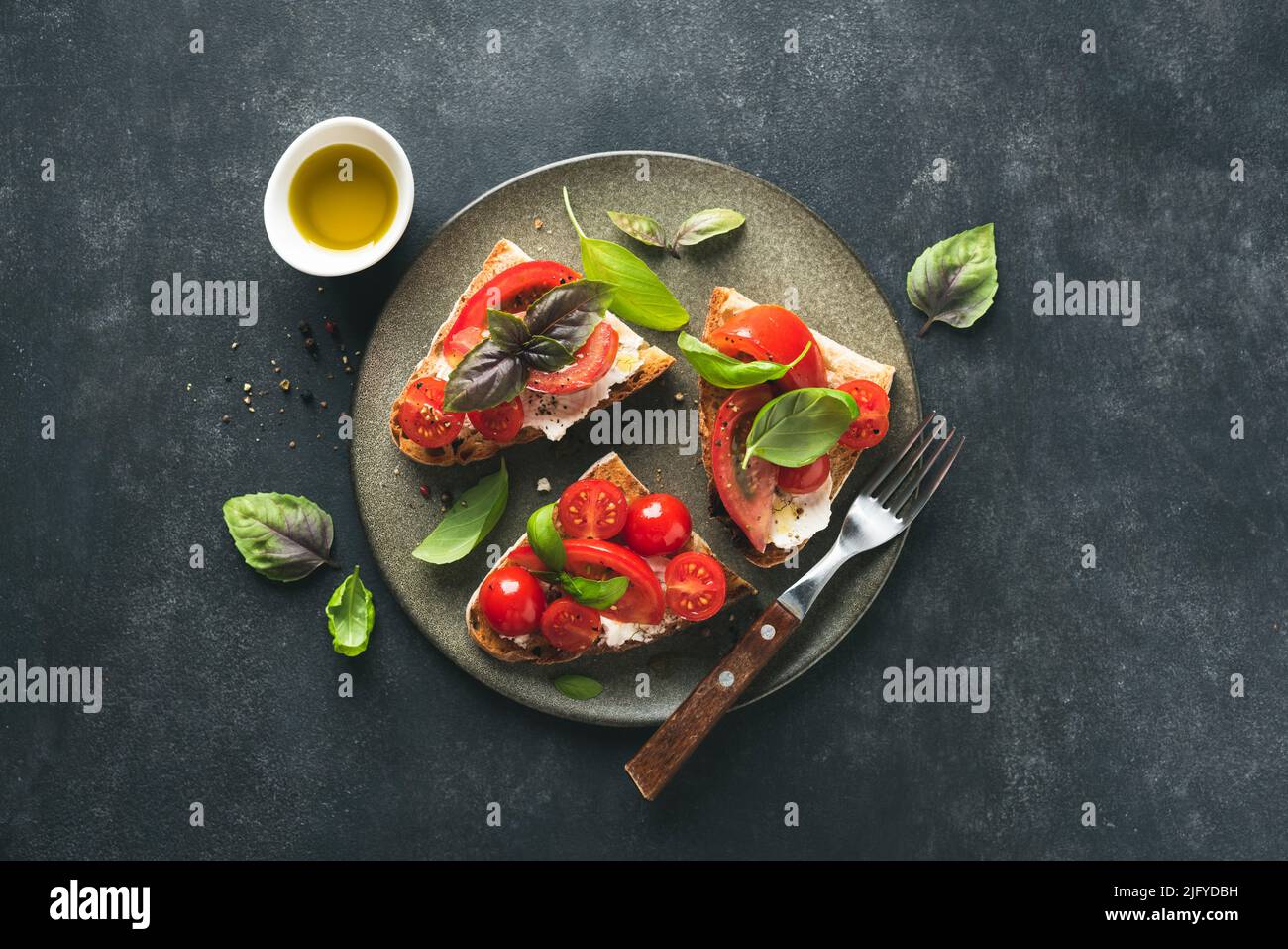 Italian tomato bruschetta with soft ricotta cheese served on a ceramic plate, top view. Dark stone background Stock Photo