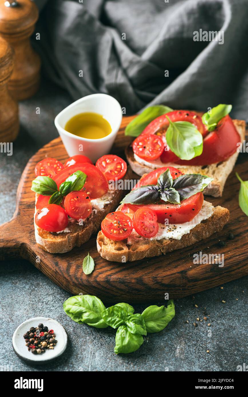 Italian tomato bruschetta with soft ricotta cheese, basil and olive oil on a wooden serving board Stock Photo