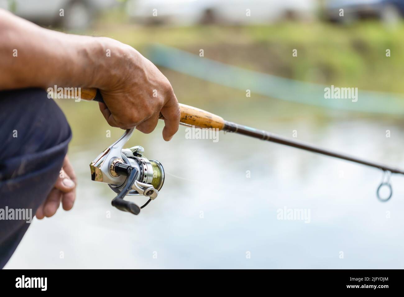 Close up fishing reel and rod in fisherman hand in a pond Stock Photo