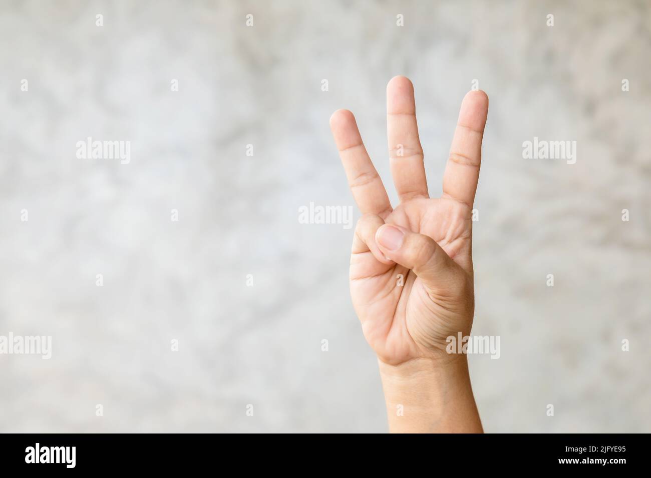 Close up hand showing three finger symbol on grey background with copy ...