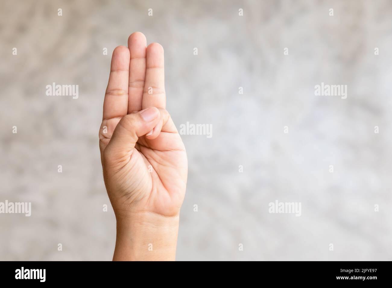 Close up hand showing three finger symbol on grey background with copy space Stock Photo