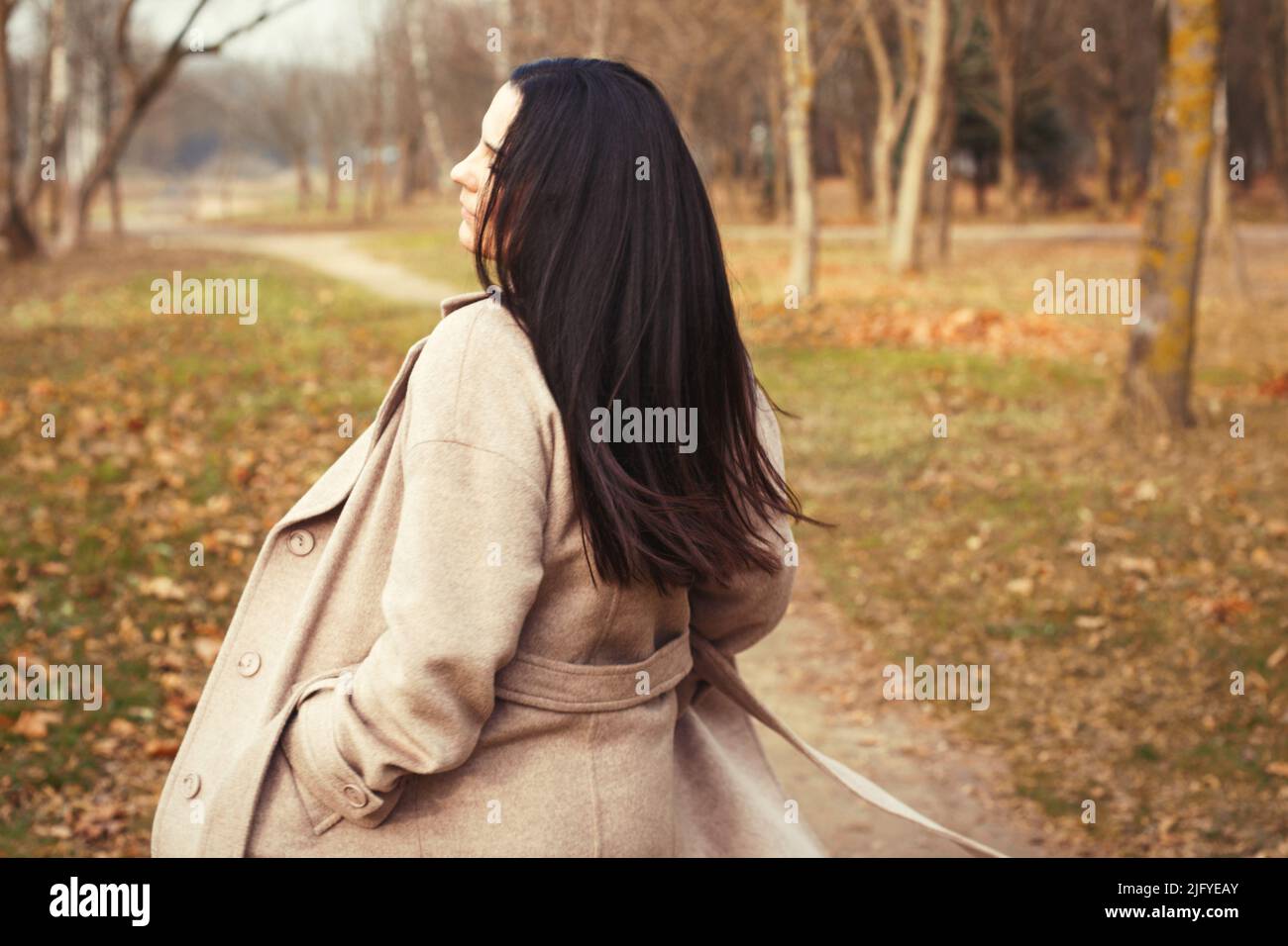 portrait of brunette hair woman in beige coat walking at the city park ...