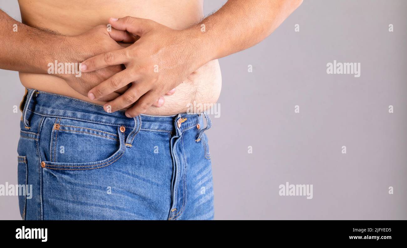 Stomach ache or pain on belly concept : Fat man using his hand and pressing on stomach on grey background Stock Photo