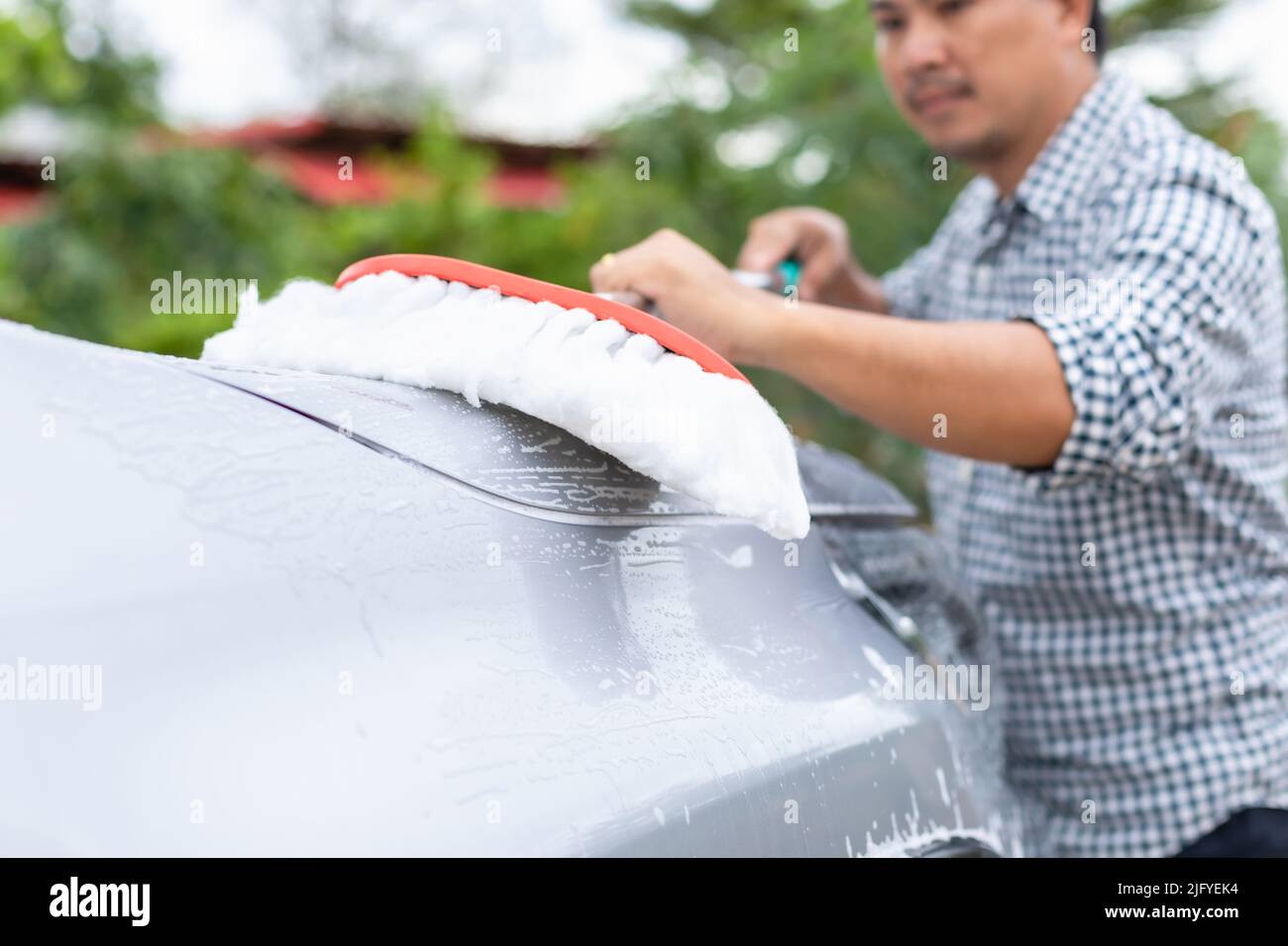 Asian man using white mop with soap to washing the car at outdoor. Car