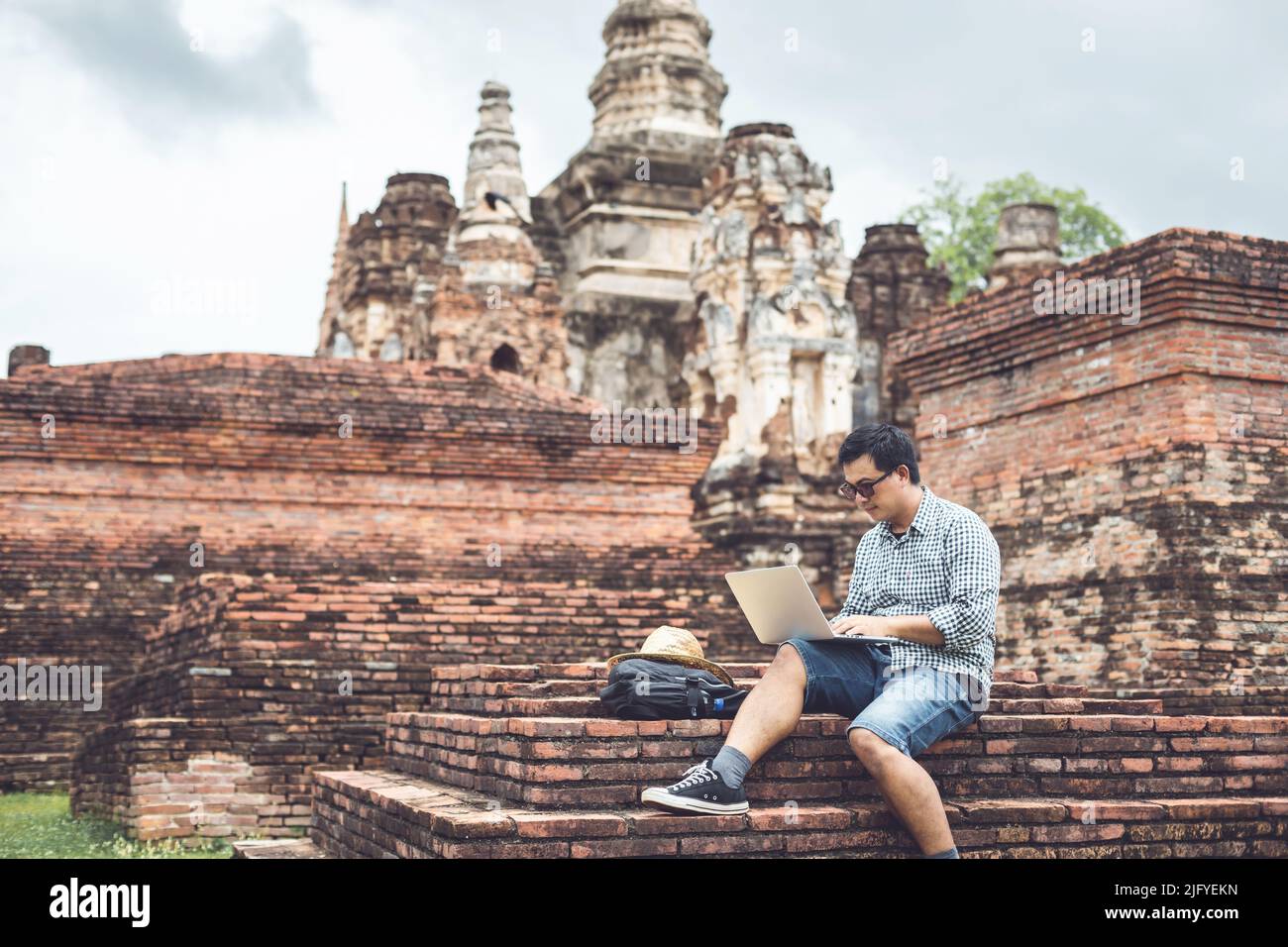 Asian tourist working and using laptop at Sukhothai historical park, Thailand. Vacation and holiday concept Stock Photo