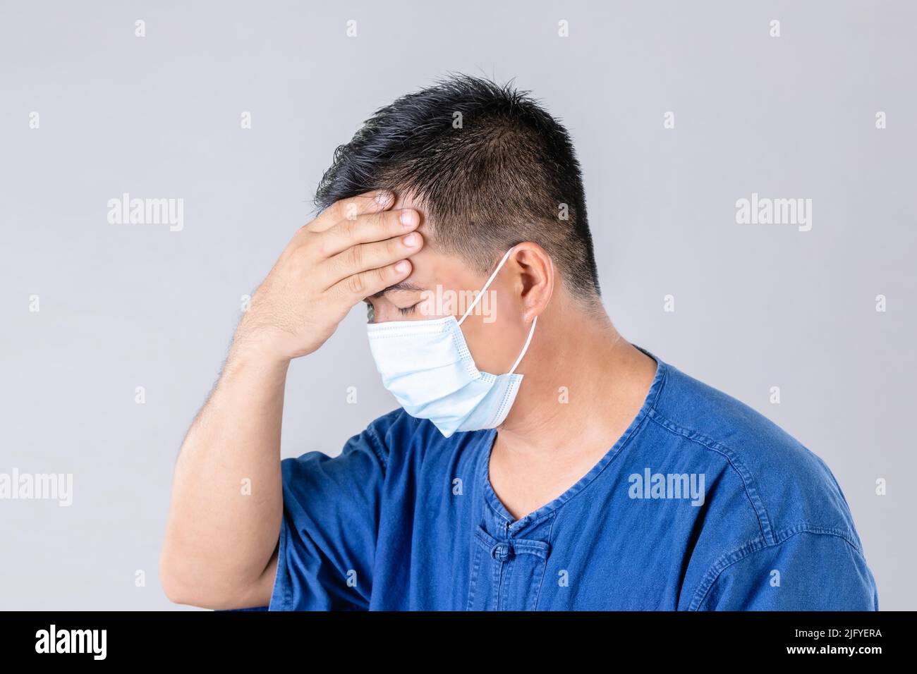 Portrait of Thai farmer wearing protective face mask to prevent virus and touch on head studio shot on grey background Stock Photo