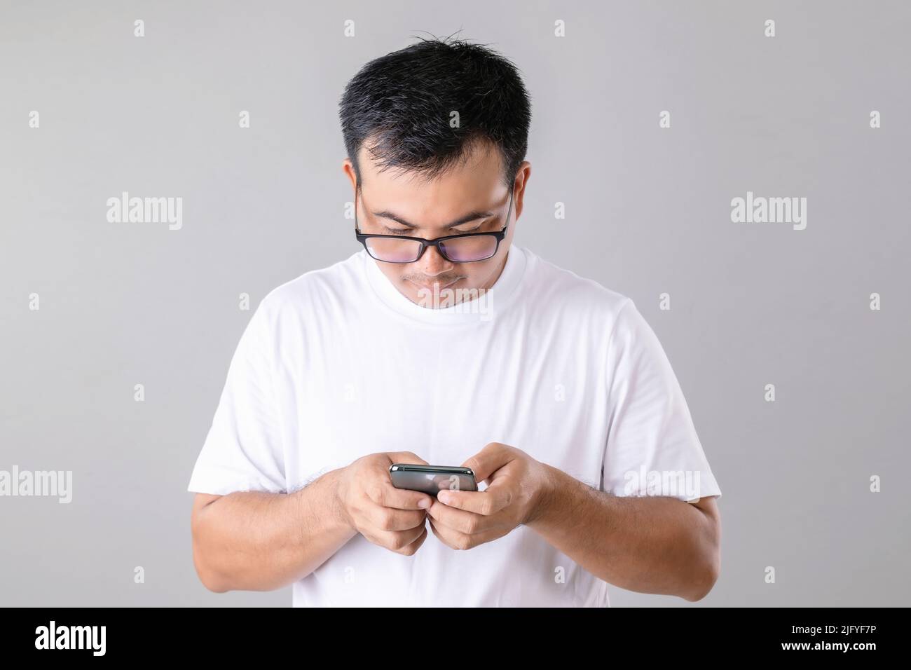 Asian man typing or chatting on smartphone studio shot on grey background Stock Photo