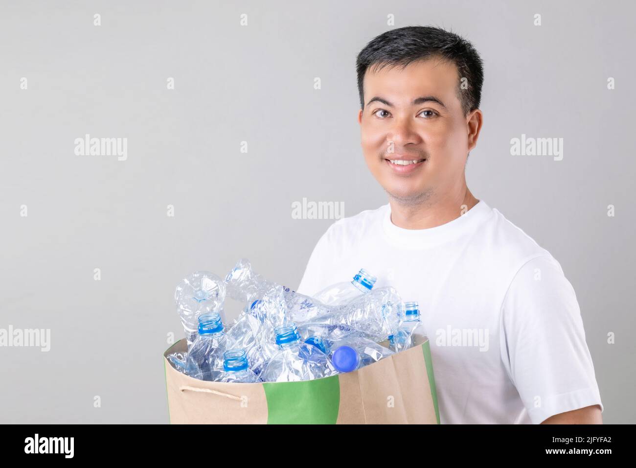 Recycle concept : Portrait Asian man holding many empty clear old water bottle. Studio shot on grey background Stock Photo