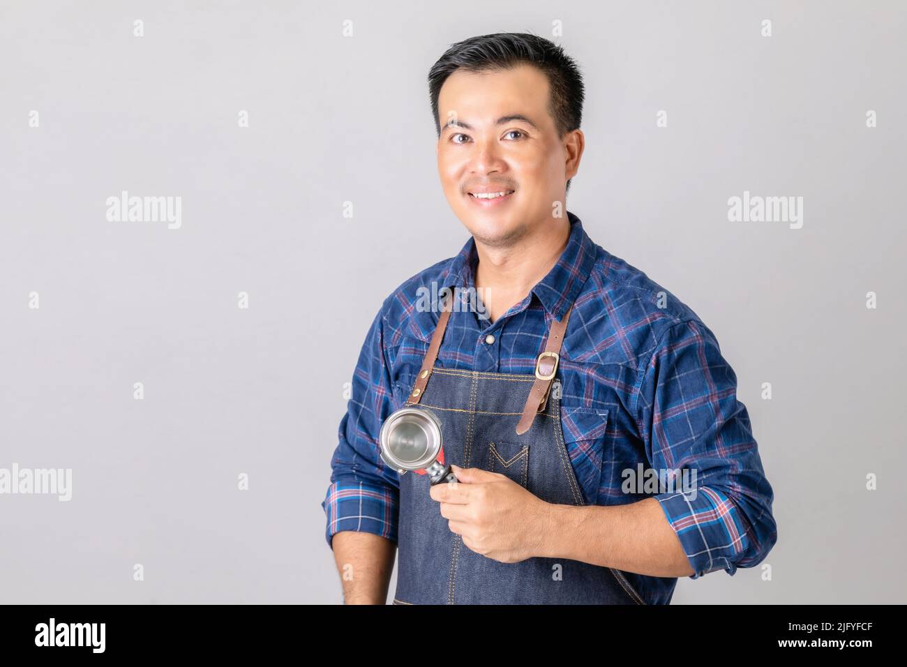 Portrait Asian man in barista uniform holding Coffee Bottomless Portafilter in studio isolated on grey background Stock Photo