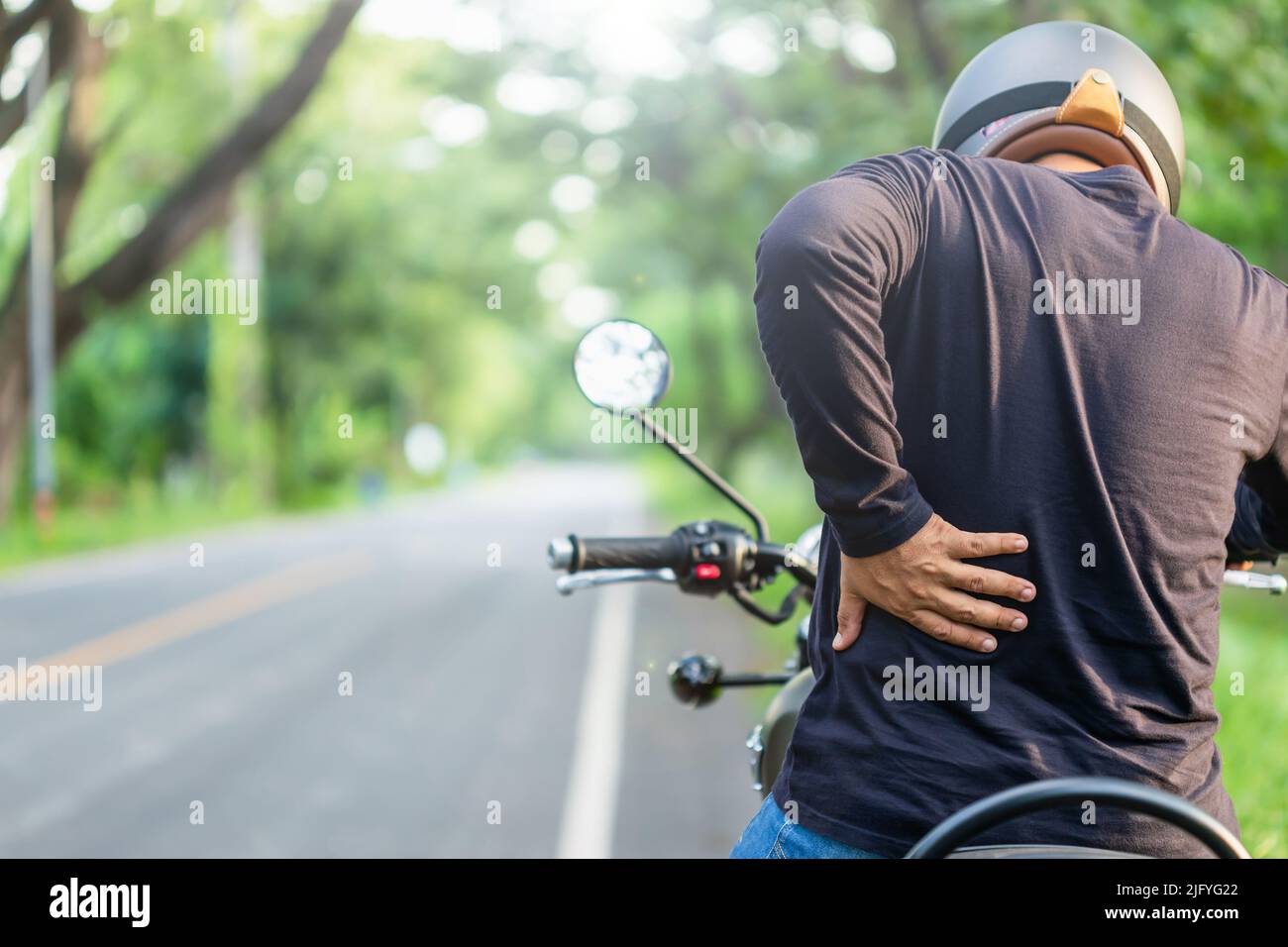Motorcyclist with pain or tired concept : Man rider touching on his back side and feeling tired after long ride motorcycle. Outdoor shooting on the ro Stock Photo
