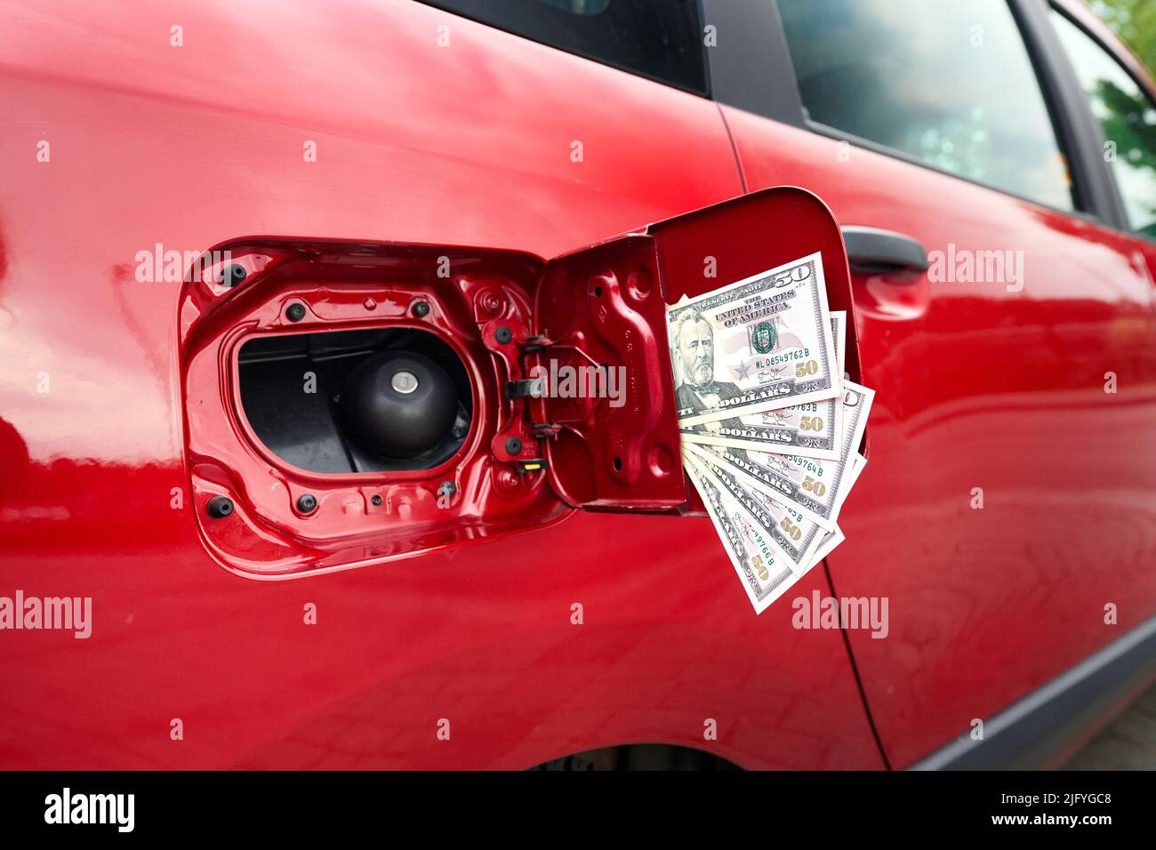 Close up of many fifty dollar bills at an open fuel tank on a car