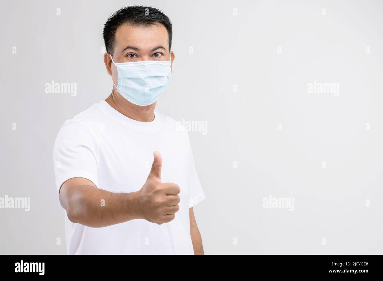 Portrait of Thai man wearing protective face mask to prevent virus studio shot on grey background Stock Photo
