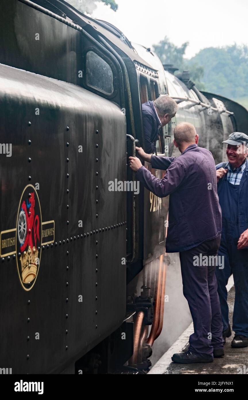 Around the UK - Engine driver leaning out of cab of BR 9F No. 92134, having a joke with his colleagues, Grosmont  Station - North Yorkshire, UK Stock Photo