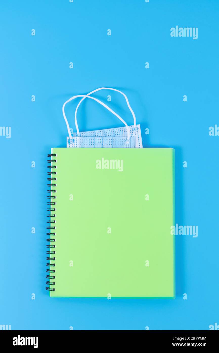 Light green copybook with blue face masks as bookmark on blue background. Post pandemic life concept. Stock Photo