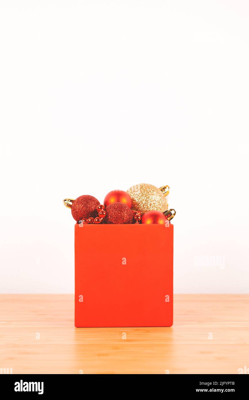 Red box with Christmas decorations against white wall. Minimal style. Copy space. Stock Photo
