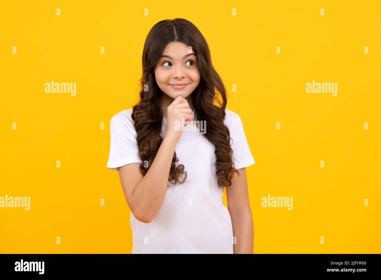 Happy teenager, positive and smiling emotions of teen girl. Smart nerdy school girl touching cheek and thinking against yellow background. Child think Stock Photo