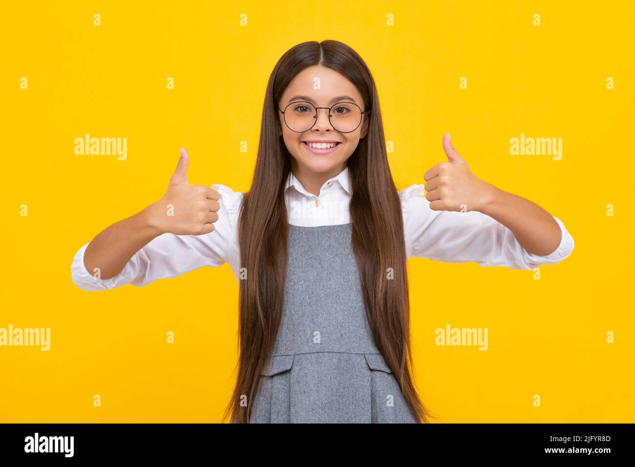 Optimistic cool teenager child girl with thumb up isolated on yellow background. Little schoolgirl student. Happy girl face, positive and smiling Stock Photo