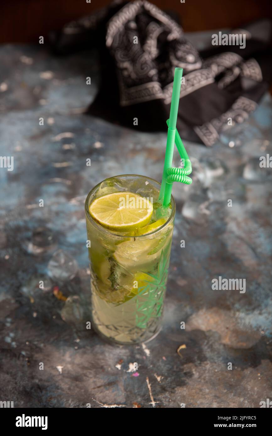 A vertical shot of a mojito glass with a green straw on a gray marble table Stock Photo