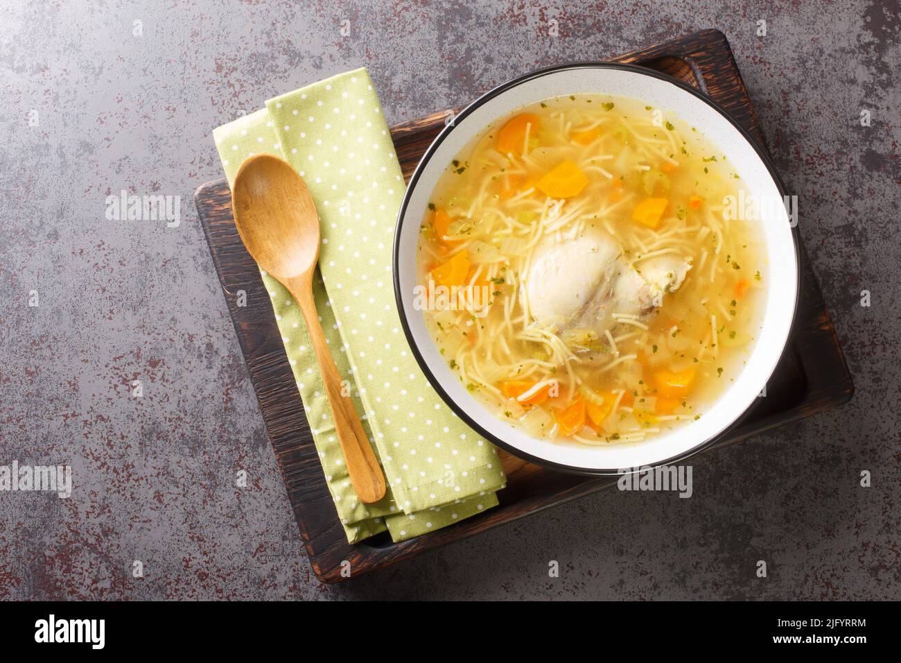 Polish Rosol z kury chicken soup with vermicelli and vegetables close-up in a bowl on a wooden tray on the table. horizontal top view from above Stock Photo