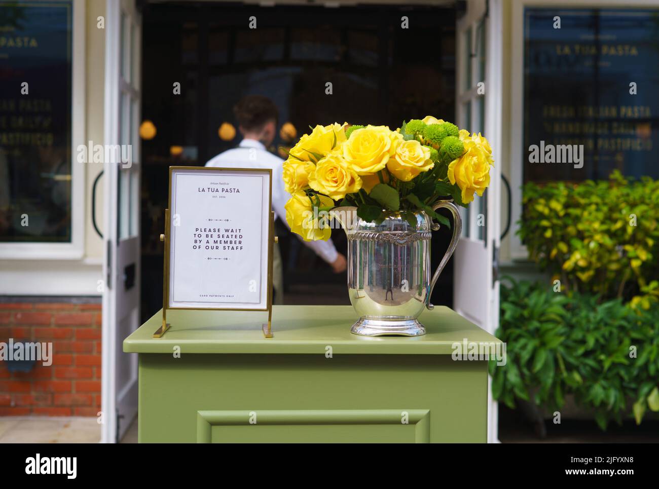 Yellow roses in a silver plated vase on a welcome lectern in front of the La Tua Pasta restaurant at Bicester Village. Stock Photo