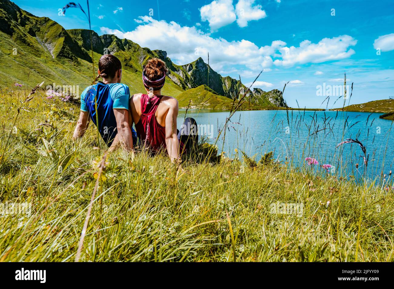A scenic view of a Caucasian couple admiring the Schrecksee lake, sitting on green grass on a sunny day Stock Photo