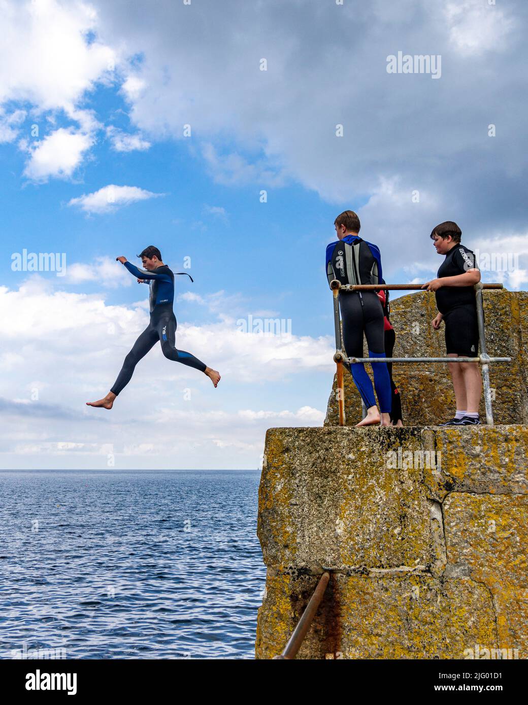 Swimmers jumping off the harbour wall at mousehole Stock Photo