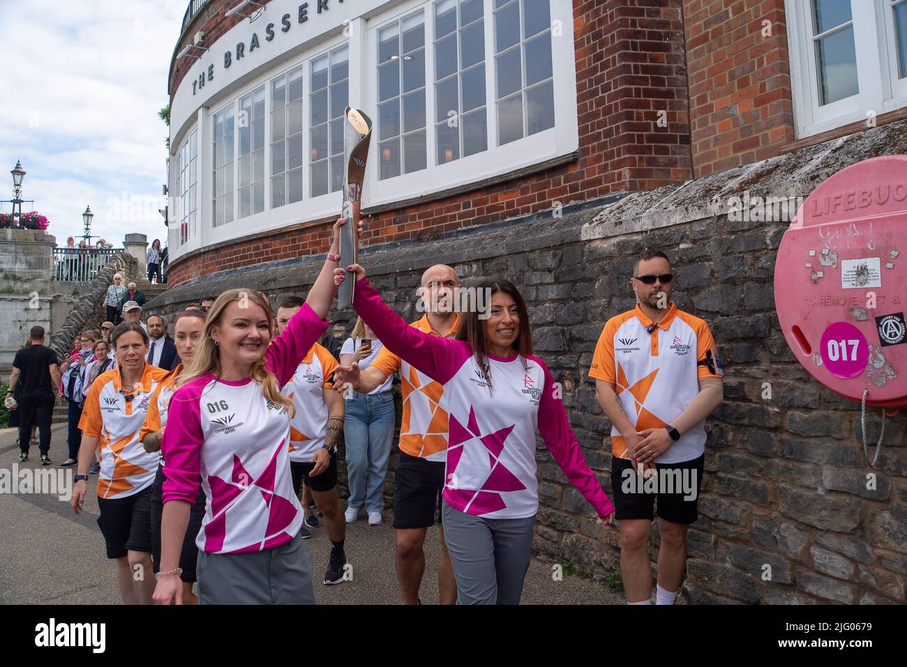 Windsor, Berkshire, UK. 6th July, 2022. Baton carrier Jemma Wood (left) takes the baton along Jennings Wharf by the River Thames into Windsor. Jemma was nominated by PwC to carry the baton. Jemma has Cystic Fibrosis and has spent 740 days of her life in hospital, 530 days devoted to nebulisers/physio and takes 720 tablets per month. Despite this, Jemma has achieved honorary life membership to the University of London gymnastics team and raised over £300,000 for the Cystic Fibrosis Trust. Credit: Maureen McLean/Alamy Live News Stock Photo