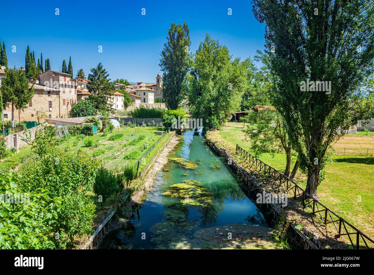 The Chiasco river that crosses the ancient medieval village of Bevagna. Perugia, Umbria, Italy. Trees, vegetation, cultivated gardens. Green algae on Stock Photo