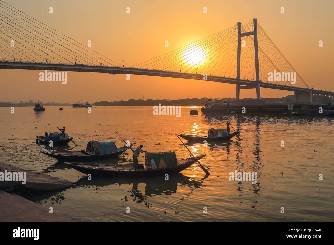 Kolkata, 20,March,2013; Reflections of local boats and Vidyasagar Setu, Bridge against setting Sun background  in river Hooghly, Kolkata, India Stock Photo