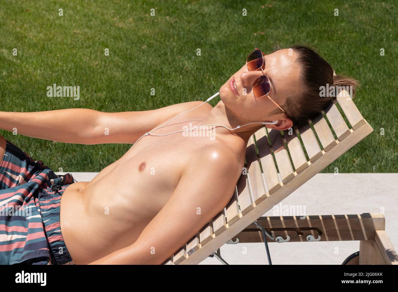 Portrait of young man relaxing sun bathing and listening to music in hot summer time Stock Photo