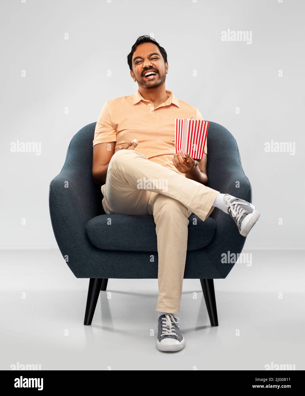 happy smiling indian man eating popcorn in chair Stock Photo